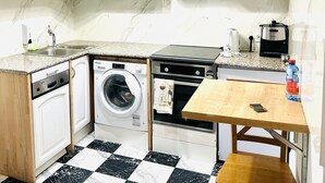 A compact kitchen with white cabinets, a washing machine, a stove, and a small dining table. - Citizen Arts Apartment in a heart of Radom (Radom)
