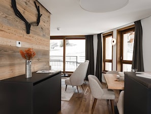 A modern kitchen with a wooden accent wall, a dining area with a table and chairs, and a view of a balcony.