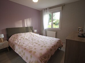 Een slaapkamer met een bed, nachtkastjes, een dressoir, een raam en een radiator.