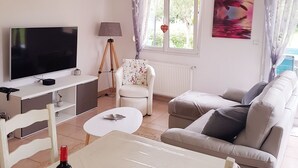 Ein Wohnzimmer mit Fernseher, Lampe, Sessel, Sofa und einem fenster mit Vorhängen.