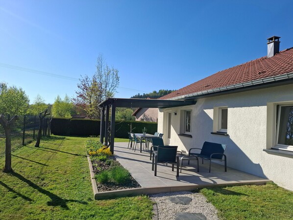 Een huis met een terras, zitplaatsen buiten en een tuin.