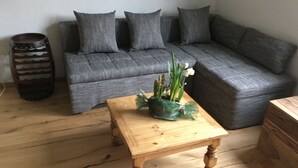 Una sala de estar con un sofá gris, una mesa de centro de madera y un jarrón verde con plantas.