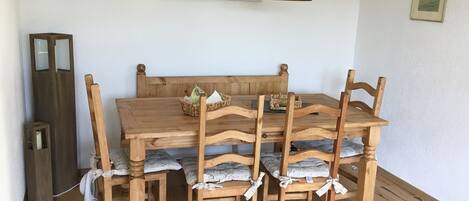 Uma mesa de jantar de madeira com seis cadeiras, uma luminária pendente preta e um quadro na parede.