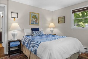 Une chambre à coucher avec un lit, deux lampes de chevet, un tableau encadré, une fenêtre donnant sur un paysage et une porte.