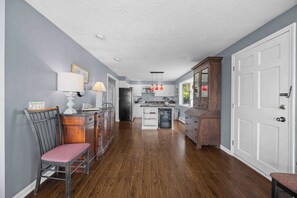 A kitchen with wooden cabinets, a dining area with a chair, and a white door. - Sunset Sanctuary: "Picture Perfect Sunsets on Canandaigua Lake!" (Canandaigua)
