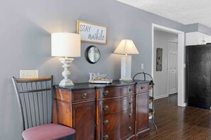 A room with a wooden cabinet, two wall-mounted lamps, a chair, and a door leading to another room. - Sunset Sanctuary: "Picture Perfect Sunsets on Canandaigua Lake!" (Canandaigua)
