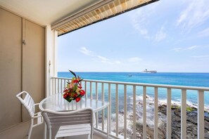 A balcony with a table and chairs, overlooking a rocky shoreline and the ocean.