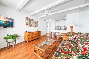 Un soggiorno moderno con un tavolino in legno, un divano con motivo tropicale, un'area pranzo e una cucina sullo sfondo.