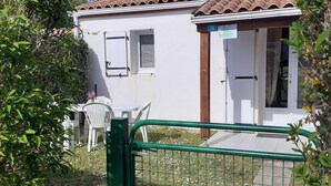 Un bâtiment blanc avec un toit recouvert de tuiles, une porte verte et une chaise blanche à l’extérieur.