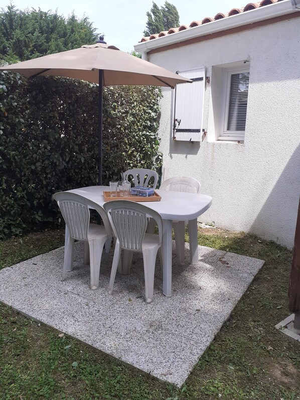 A patio with a table and chairs, a table umbrella, and a window with blinds. - 3* furnished accommodation for curists or holidaymakers -discover the Haute Saintonge region (Ozillac)