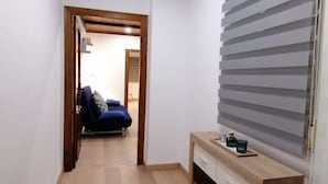 A narrow hallway with a wooden ceiling, a bed with blue bedding, and a wooden console table with drawers. - Spacious Apartment (Armilla)