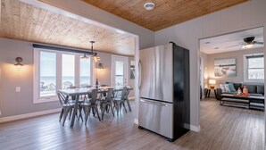 Una cocina amplia con refrigerador de acero inoxidable, techo de madera y ventanas grandes con vistas a un paisaje rocoso.