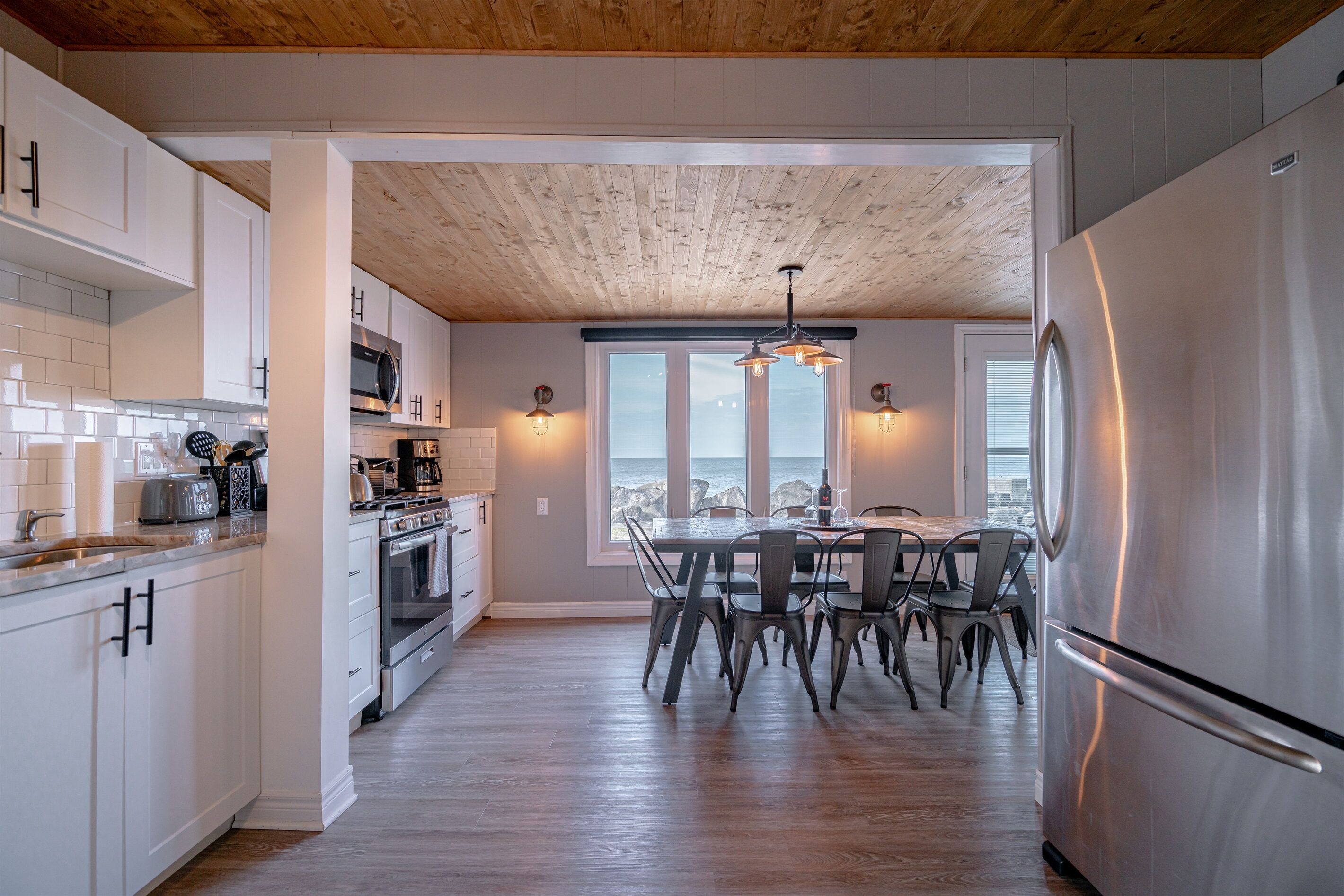 Une cuisine moderne avec des meubles blancs, des appareils en acier inoxydable et un coin repas comprenant une table et des chaises en bois.