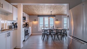 Una cocina moderna con armarios blancos, electrodomésticos de acero inoxidable y una zona de comedor con mesa y sillas de madera.
