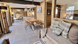Un amplio salón con una mesa de comedor de madera, un sofá con cojines escoceses y un gran ventanal que proporciona luz natural.