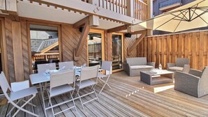Una terraza al aire libre con piso de madera, mesas plegables blancas y sillas con cojines grises.