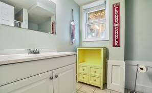 A bathroom with a white sink, a yellow cabinet, a mirror, and a toilet paper holder. - Changes In Latitude: Spacious 6BR, 4BA home in Holden Beach, perfect for 14 guests. (Holden Beach)