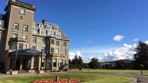 A large, historic building with a prominent entrance, a well-maintained lawn, and a clear sky.