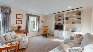 A living room with a sofa, armchairs, a wooden coffee table, a TV, and a bookshelf.