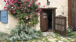 Ein rustikales Gebäude mit einer Holztür, einem kleinen Garten mit rosa Rosen und einem Kiesweg.