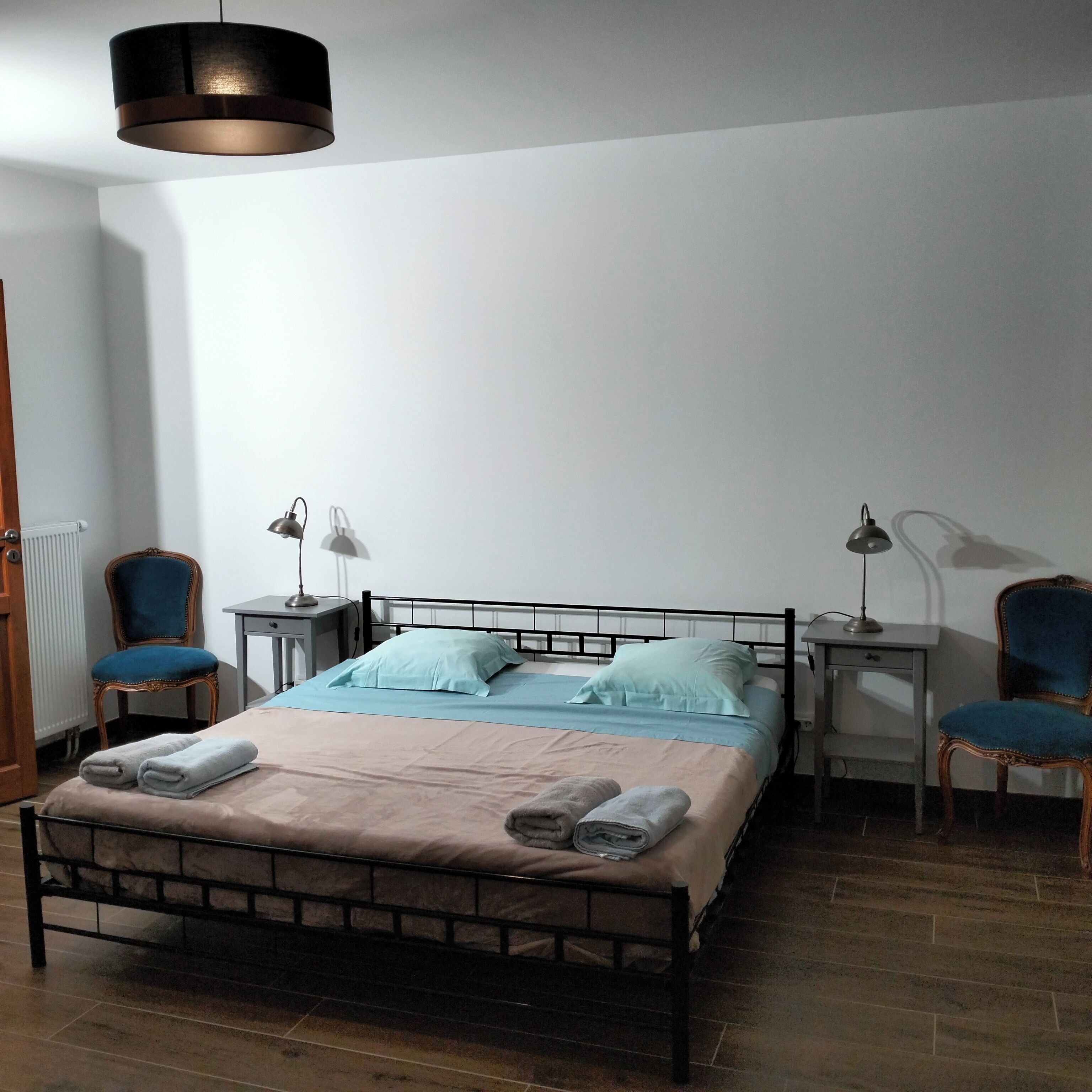Ein ordentlich eingerichtetes Schlafzimmer mit einem Bett, zwei Sesseln, zwei Schreibtischen und einer Pendelleuchte.
