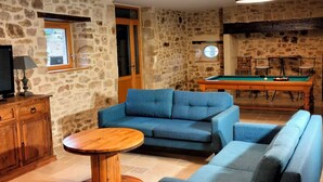 A cozy living room with a stone wall, a pool table, a sofa, and a television. - Gîte des 3 pays, ideal for reunions with family or friends (cublac)