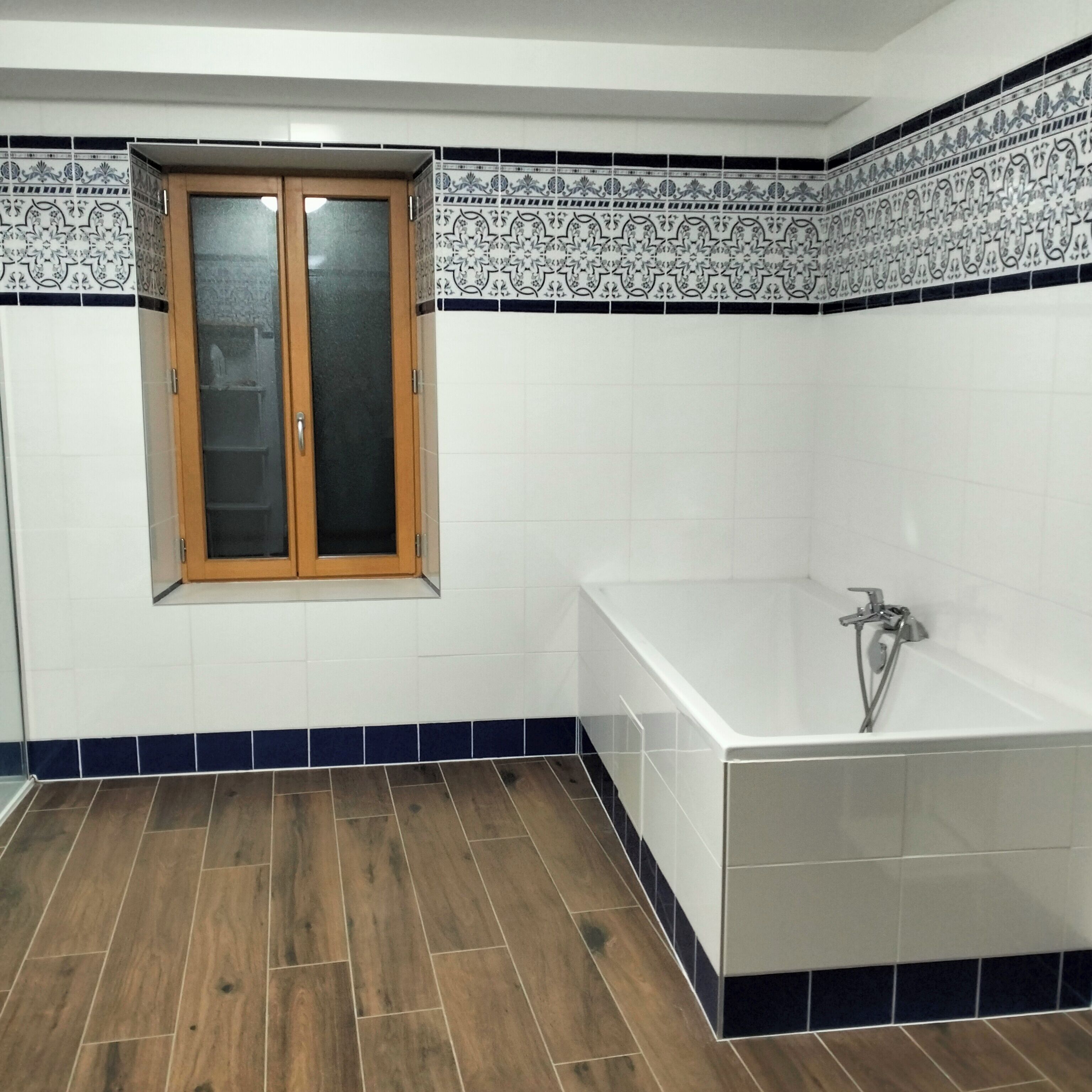 Ein Badezimmer mit Holztür, einer Badewanne und gemusterten Fliesen.