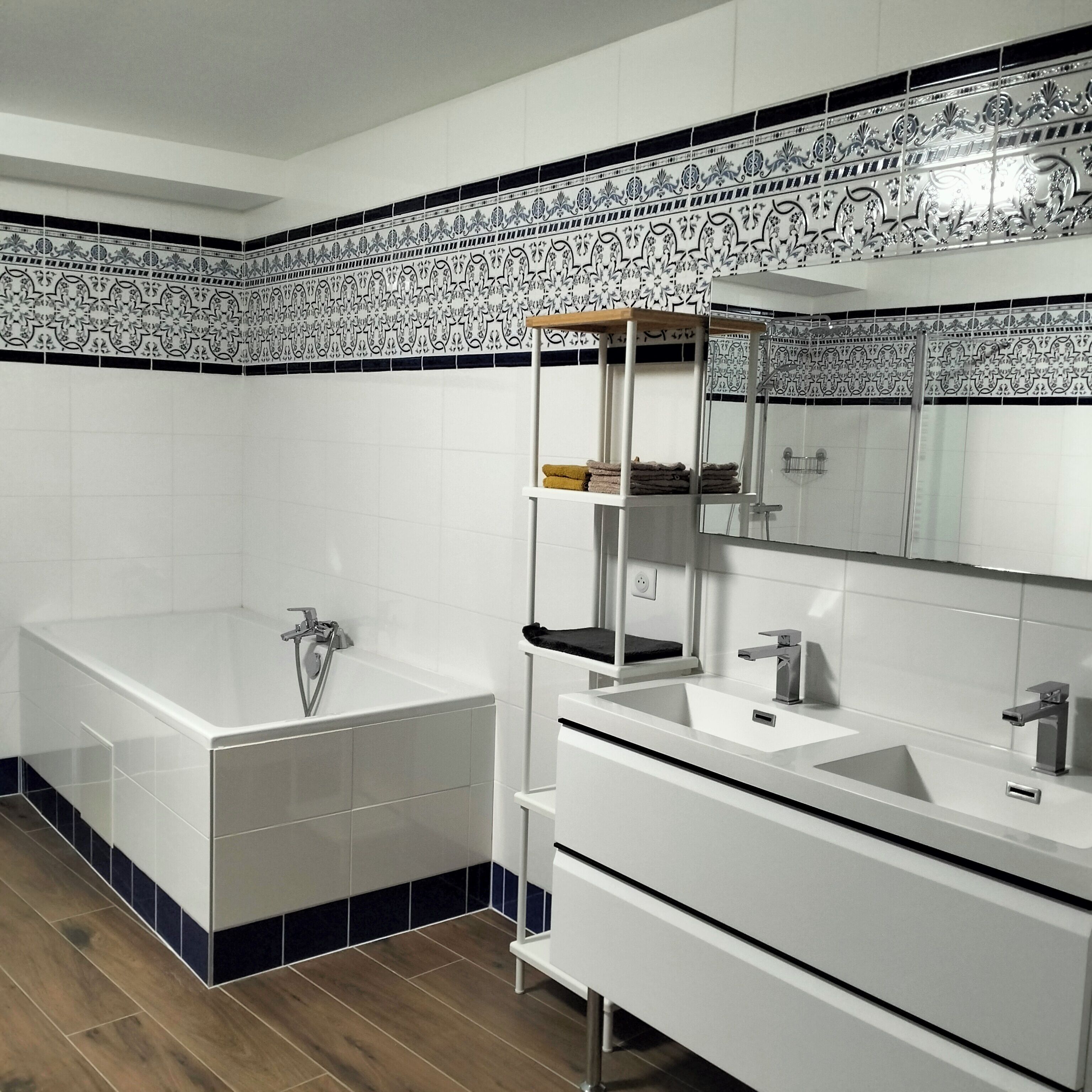 A modern bathroom with a bathtub, a sink, and a mirror. There is a shelf with towels and a showerhead.