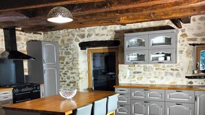 A kitchen with a central island, grey cabinets, a stone wall, and a hanging light fixture. - Gîte des 3 pays, ideal for reunions with family or friends (cublac)