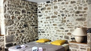 A room with a stone wall, a bed with a wooden frame, a lamp on a side table, and a wooden floor. - Gîte des 3 pays, ideal for reunions with family or friends (cublac)