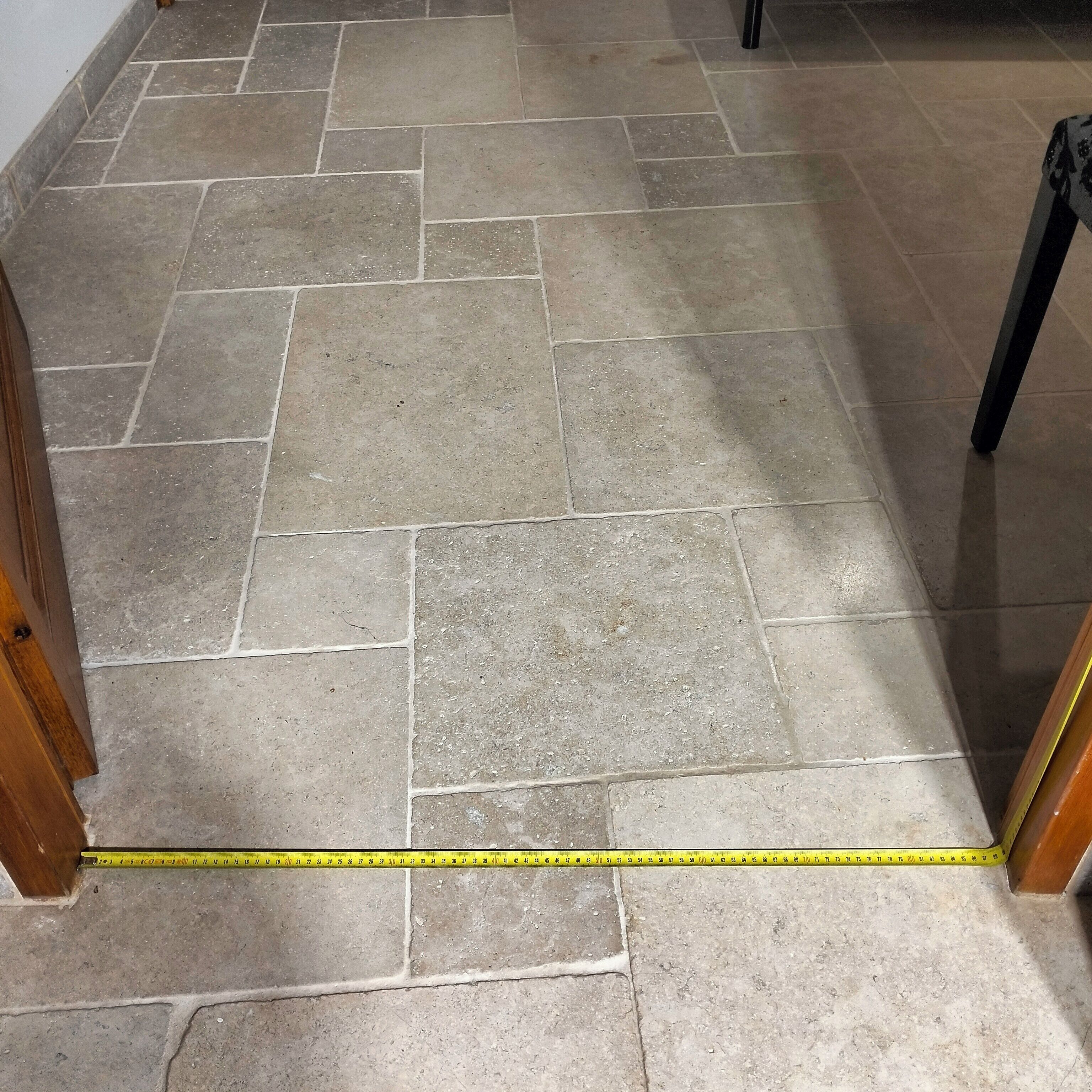 Une pièce dont le sol est recouvert de carreaux, mesurant 3,6 mètres sur 3,6 mètres, et où un mètre ruban indique les dimensions.