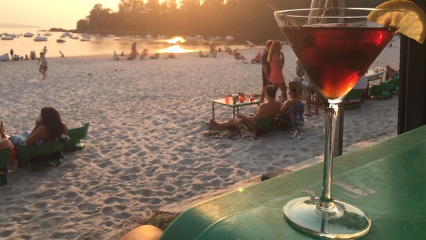 Una spiaggia con persone che si rilassano e un cocktail in un bicchiere.
