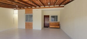 A spacious room with a tiled floor, wooden ceiling beams, and two windows with metal bars.