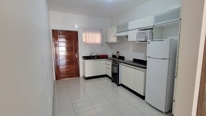 A kitchen with white cabinets, a microwave, a refrigerator, and a wooden door.