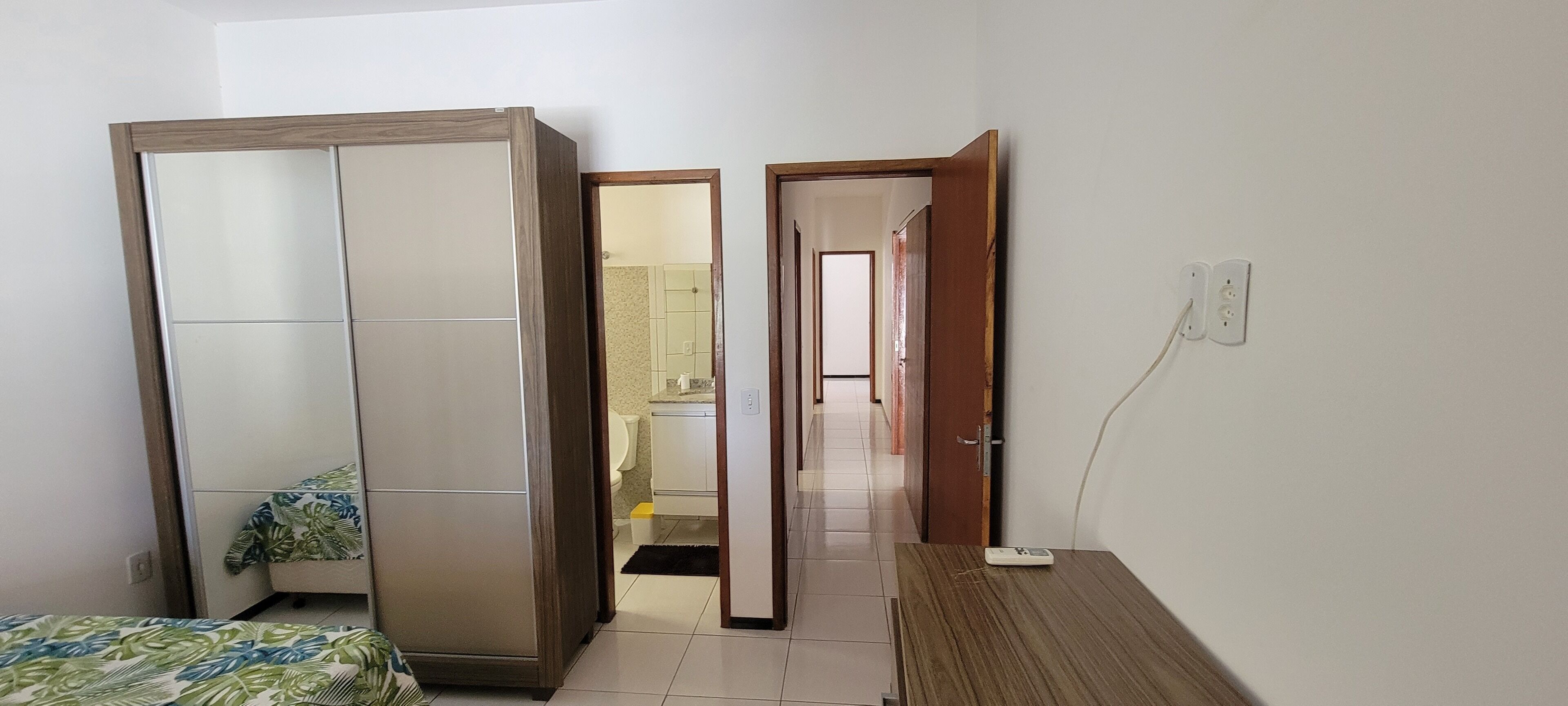 A bedroom with a wardrobe, a bed with a patterned bedspread, a bedside table, and a mirror.