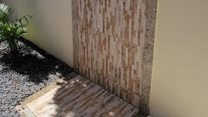 A modern outdoor shower area with a wooden panel design, a metal handrail, and a tiled floor.