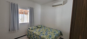 A small bedroom with a single bed, a window with curtains, and an air conditioning unit.
