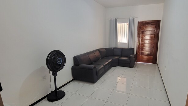 A room with a black leather sofa, a standing fan, a wooden door, and a window with curtains.