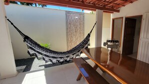 A hammock, a table, a bench, and a door in a room with tiled flooring and a white wall.