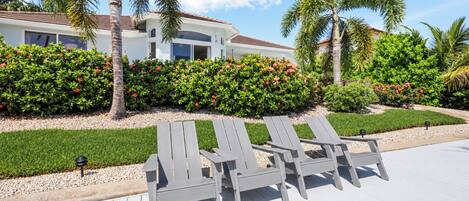 A resort with a poolside area featuring lounge chairs and a well-maintained garden with palm trees and flowering bushes.