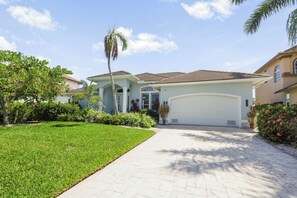 A residential property with a paved driveway leading to a garage, surrounded by well-maintained lawns and various plants.