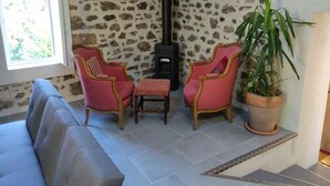 Ein Wohnzimmer mit einer Steinsäule, zwei rosafarbenen Sesseln, einem kleinen Tisch, einem Sofa, einer Topfpflanze und einem Kamin.
