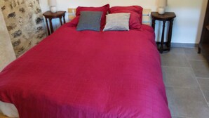 Ein Bett mit roter Bettdecke und zwei Kissen, an beiden Seiten jeweils ein Nachttisch mit Lampe.