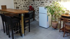 Eine kleine Küche mit einem Holztisch, schwarzen Stühlen, einem weißen Kühlschrank und einem Blumentopf.