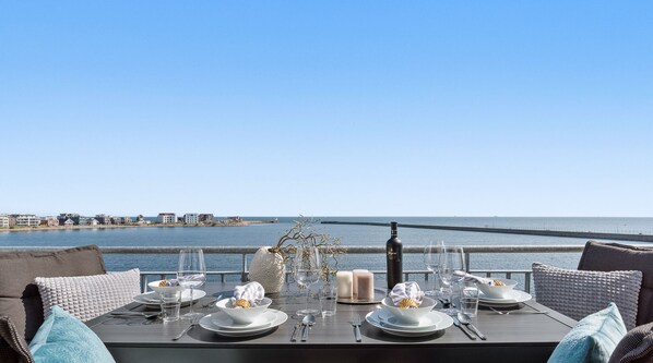A table set for dining with a view of the sea and buildings in the distance. - Seewind - Balcony, garden furniture,fireplace,washing machine,underfloor heating (Olpenitz)