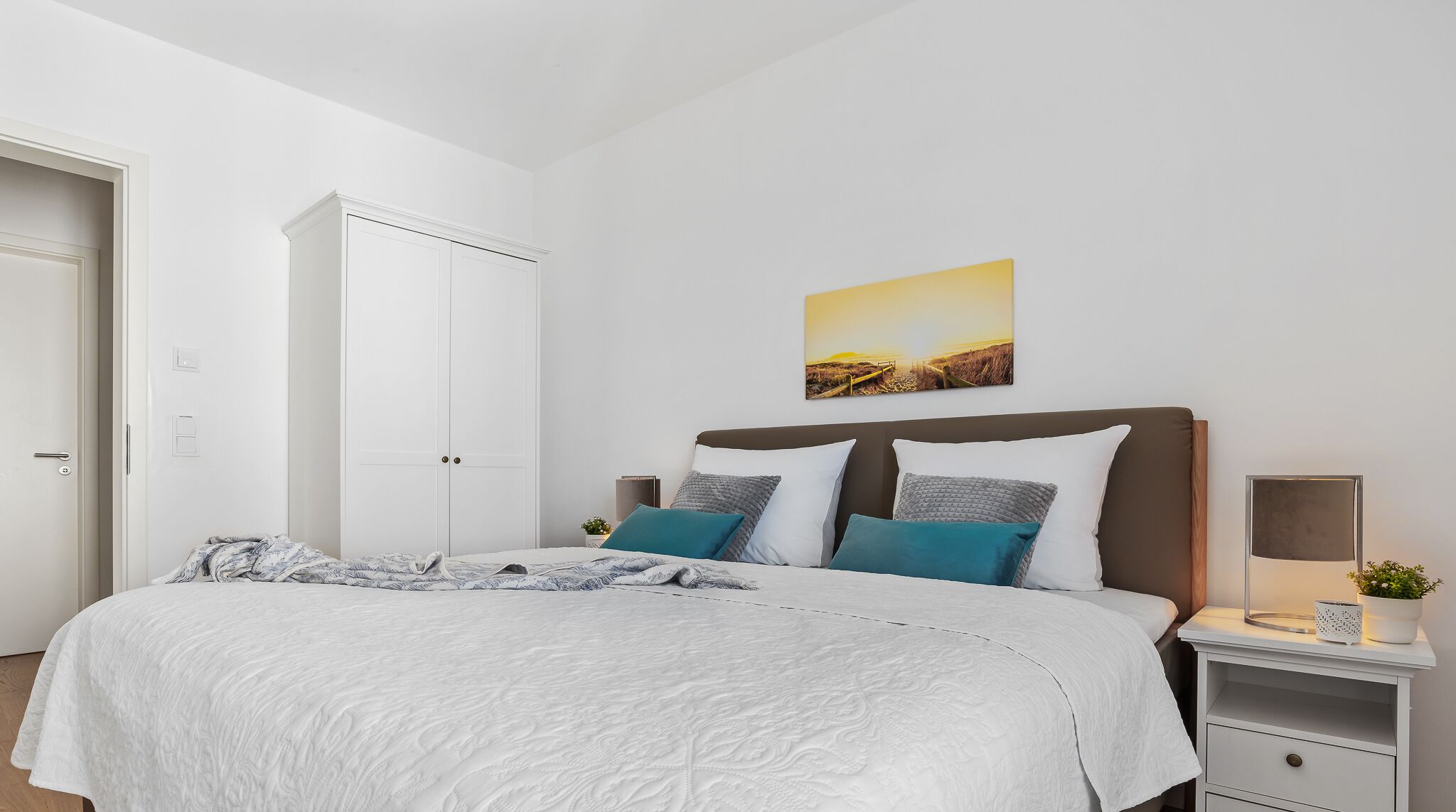 A bedroom with a bed, a nightstand, a bedside table, a wall-mounted lamp, and a door.