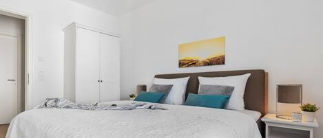 A bedroom with a bed, a nightstand, a bedside table, a wall-mounted lamp, and a door.
