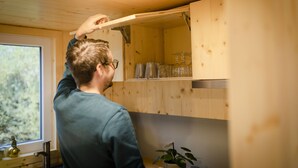 Une personne ouvre une armoire en bois dans une pièce dotée d’une fenêtre et d’une plante posée sur le rebord de la fenêtre.