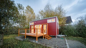 Une cabane rouge dotée d’une terrasse en bois et d’un petit escalier menant à l’entrée.