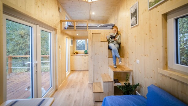 Une petite cabane dotée d’un lit en mezzanine, d’une kitchenette et d’une grande fenêtre offrant une vue sur l’extérieur.